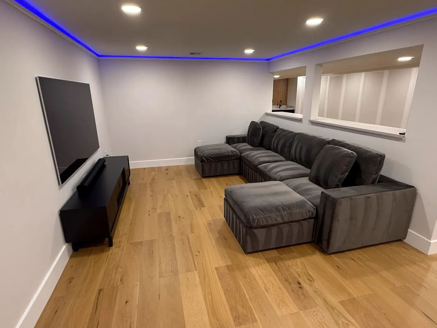 Finished basement media room by MG Builders with a wall-mounted TV, recessed lights and an LED ceiling strip